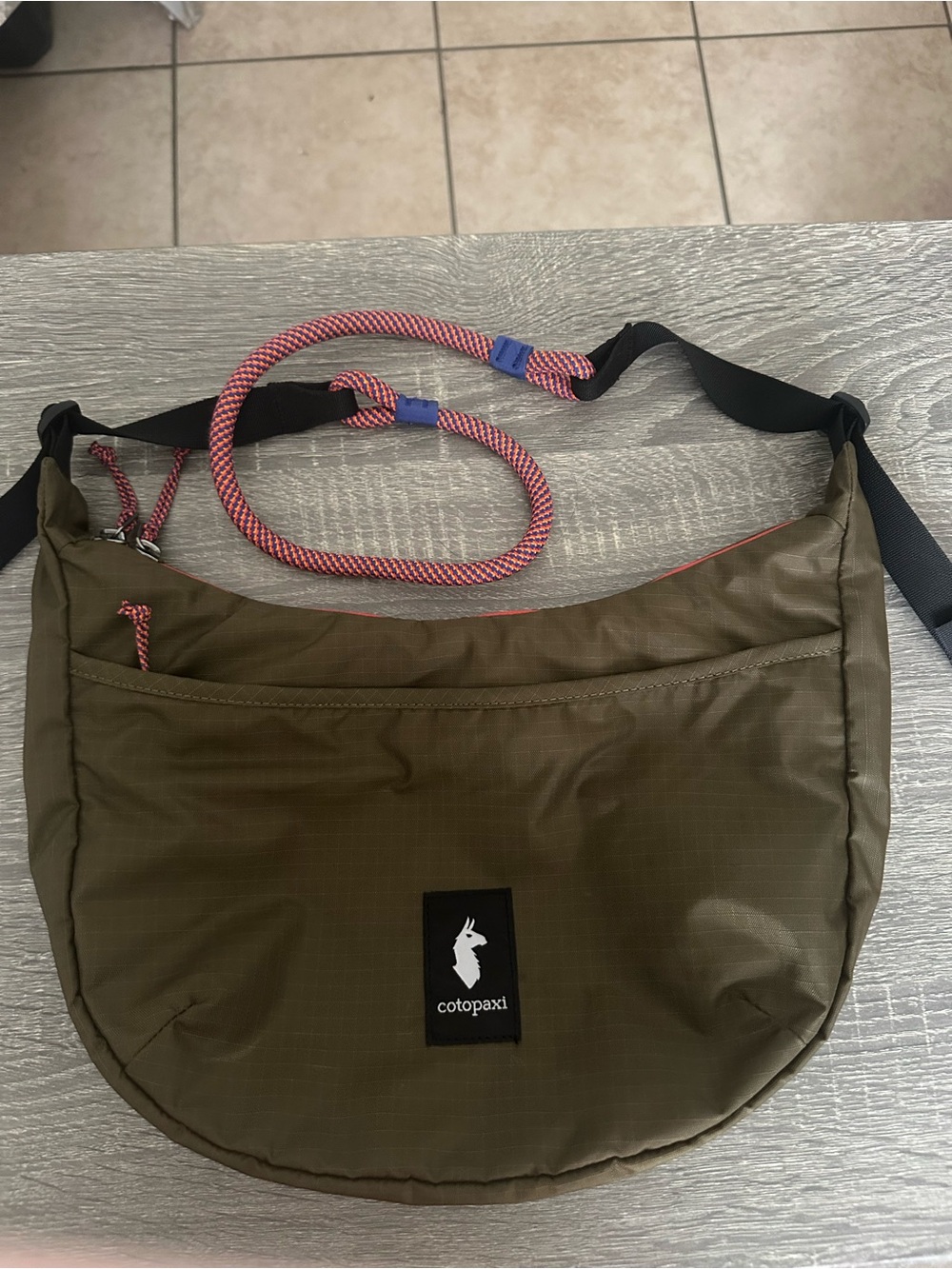 cotopaxi olive green sling bag with red-accent cord